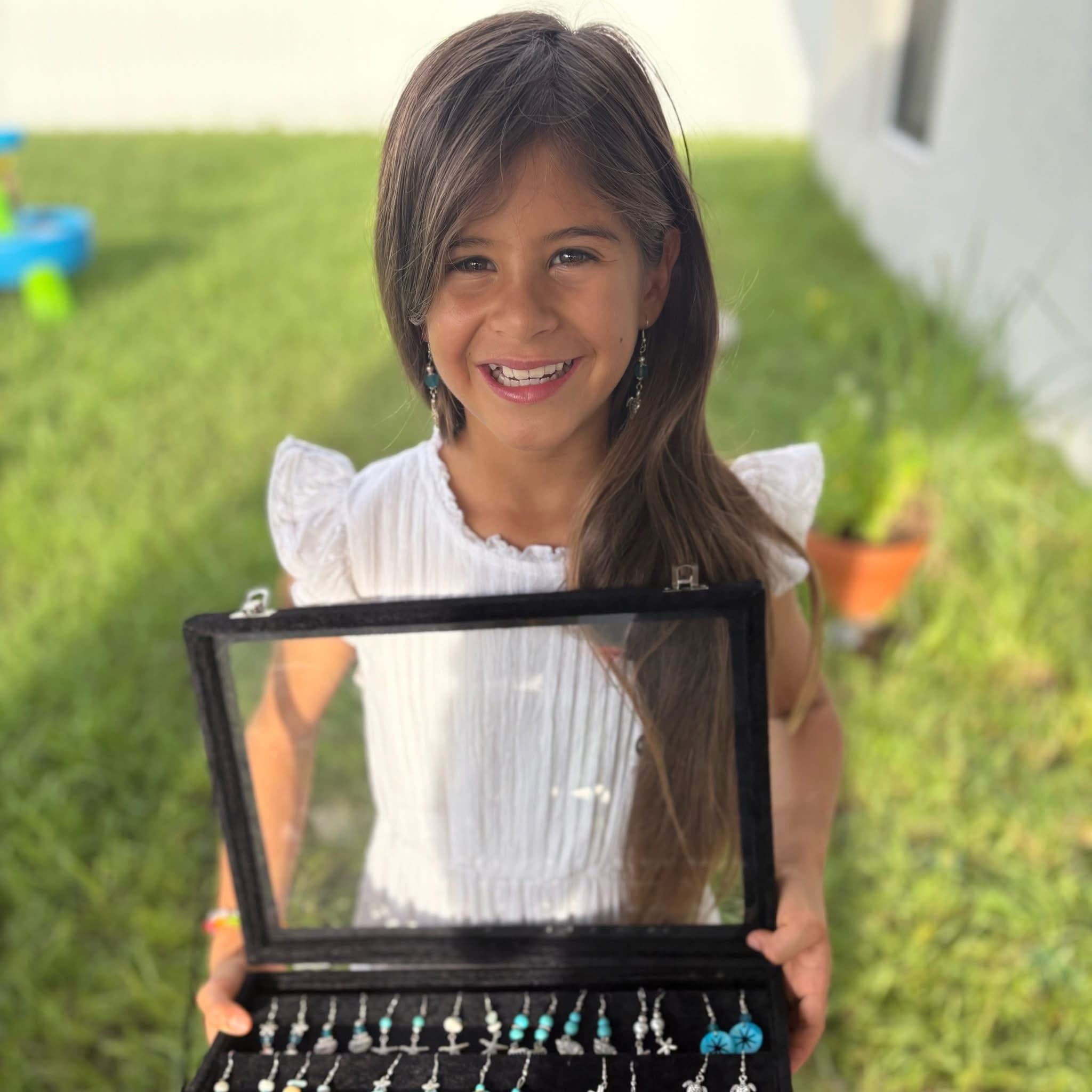 Naomi, age 9, holding a case of her handmade earrings